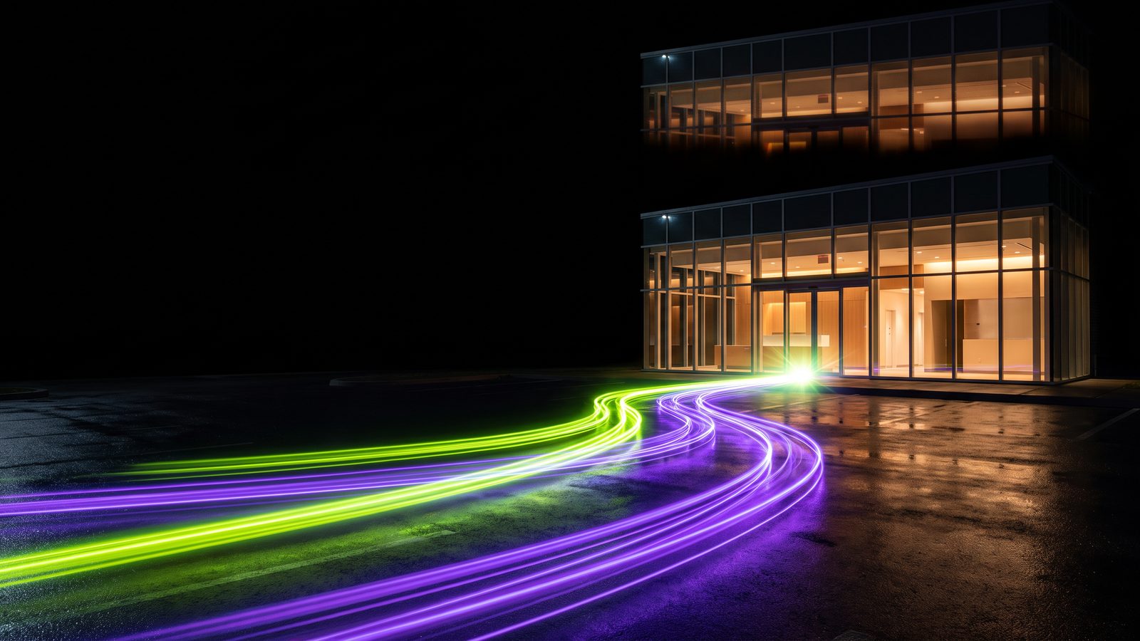 Two streams of light, one green and one violet, converging on the glass entrance of a modern clinic at night.