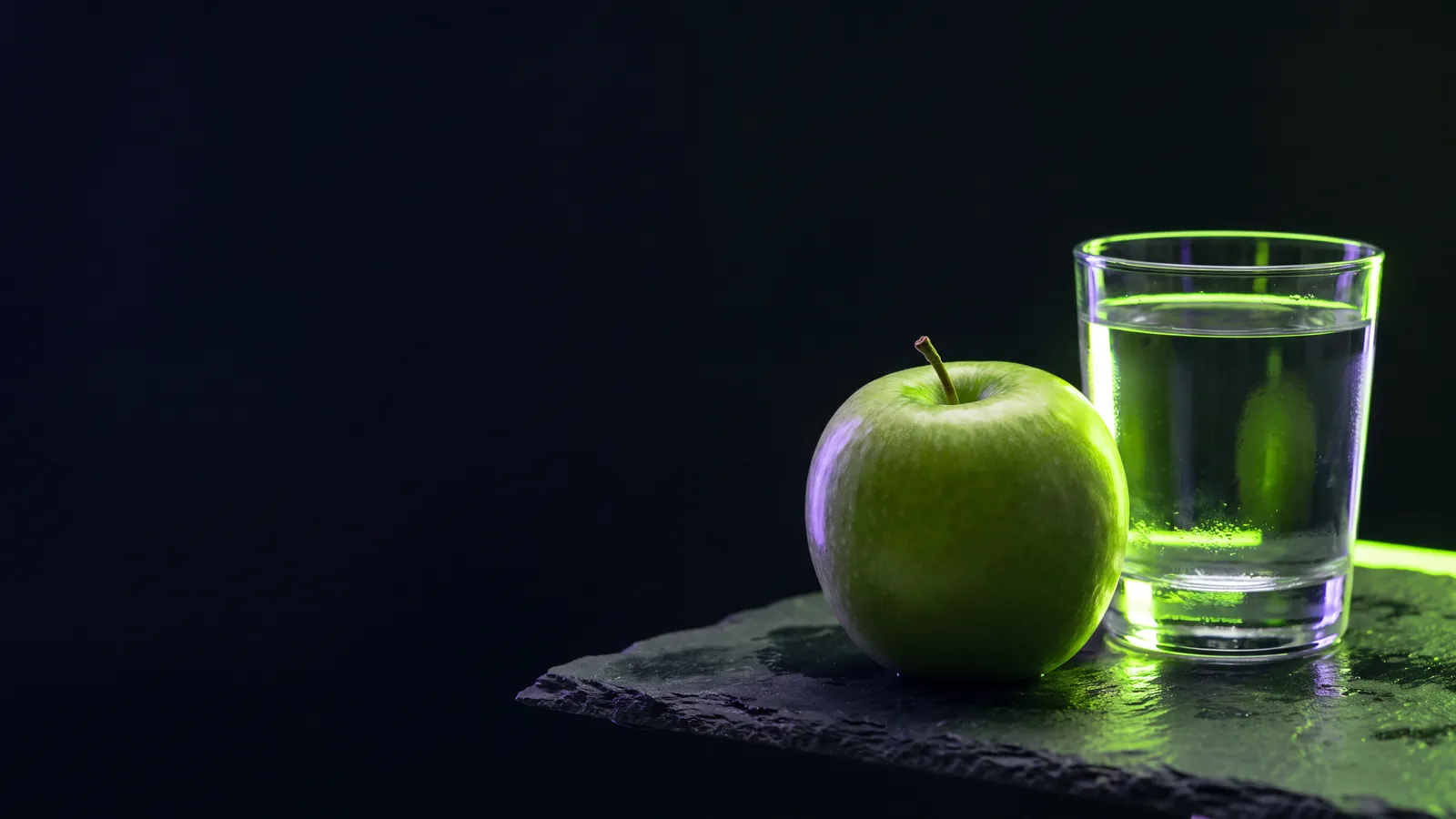 Concept render: a green apple beside a glass of water on slate